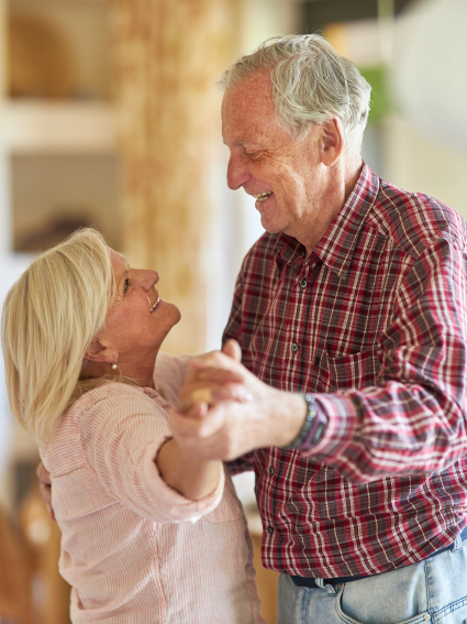 Older adult couple dancing in their home while looking lovingly at each other