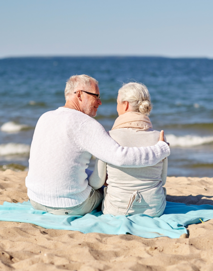 Elderly couple sitting on beach blanket and looking out at ocean