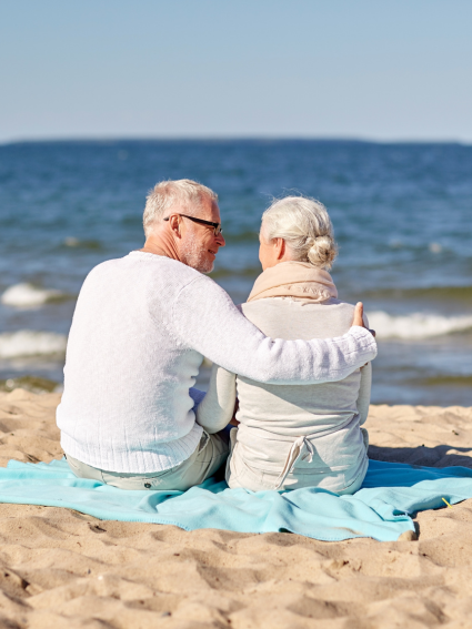 Elderly couple sitting on beach blanket and looking out at ocean