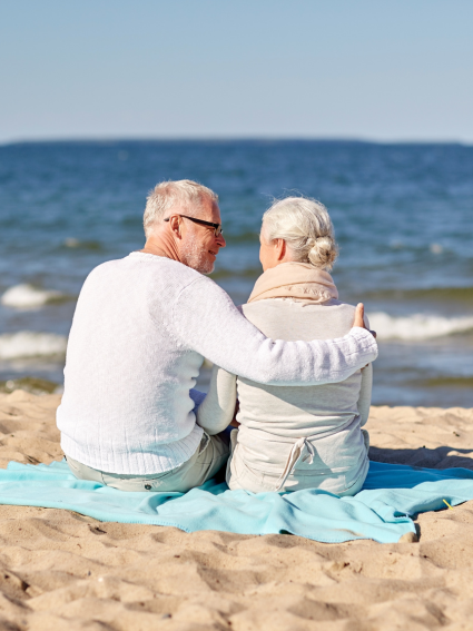 Older adult couple sitting on a blanket and looking out at the ocean