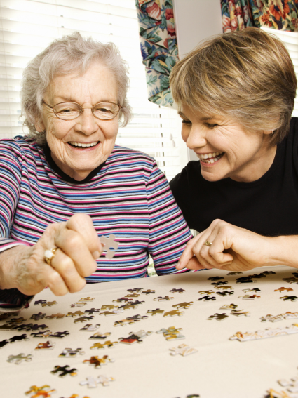 Elderly woman and middle aged woman smiling as they work on a puzzle together