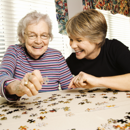 Elderly woman and middle aged woman smiling as they work on a puzzle together