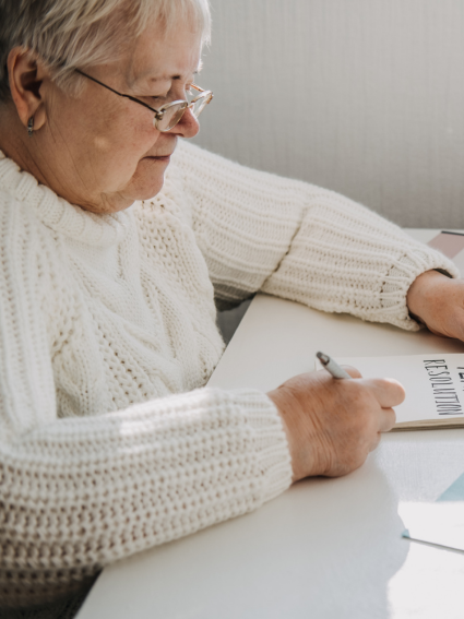 Older adult woman in white sweater at a desk - writing her New Year resolutions