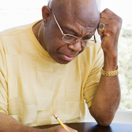 Older adult black male wearing a yellow t-shirt and concentrating on a crossword puzzle